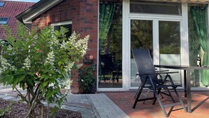 A house with a brick exterior, large windows, and a patio area with a chair and table.