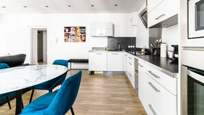 A modern kitchen with white cabinets, a black countertop, and a marble dining table with blue chairs. - Le Gilbert 1 - 10 impasse Gilbert - Vichy (Vichy)