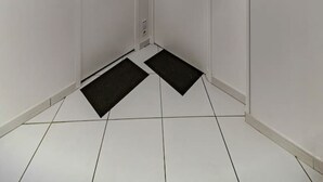 A clean, white-walled hallway with two doors, a small light fixture, and black doormats on the floor. - Le Gilbert 1 - 10 impasse Gilbert - Vichy (Vichy)