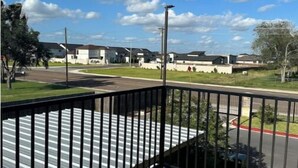 A balcony with a metal railing overlooking a residential area with houses and a clear sky. - Lemon Home - 2 Queen BR (Edinburg)