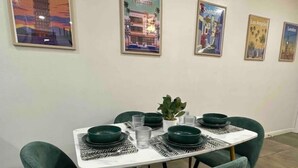A dining area with a white table and green chairs, framed cityscape pictures on the wall, and a small potted plant on the table. - Lemon Home - 2 Queen BR (Edinburg)