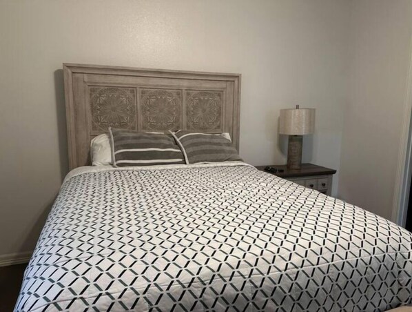 A bed with a geometric patterned bedspread, a wooden headboard, and two pillows.