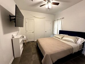 A bedroom with a bed, a desk, a chair, a ceiling fan, and a TV mounted on the wall.