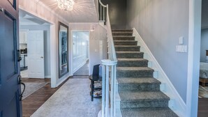 Un intérieur de maison comprenant un escalier, un couloir menant à la cuisine et un espace de vie.