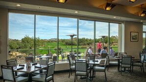 A dining area with large windows offering a view of a golf course. Tables and chairs are arranged for dining. - Troon North Private Pool & Spa (Scottsdale)