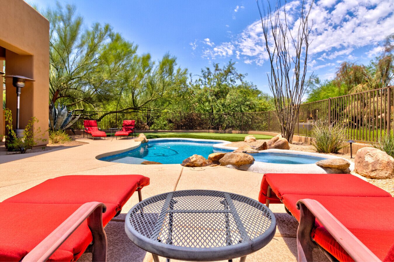 Un jardin avec une piscine, des chaises longues rouges et une table en métal.