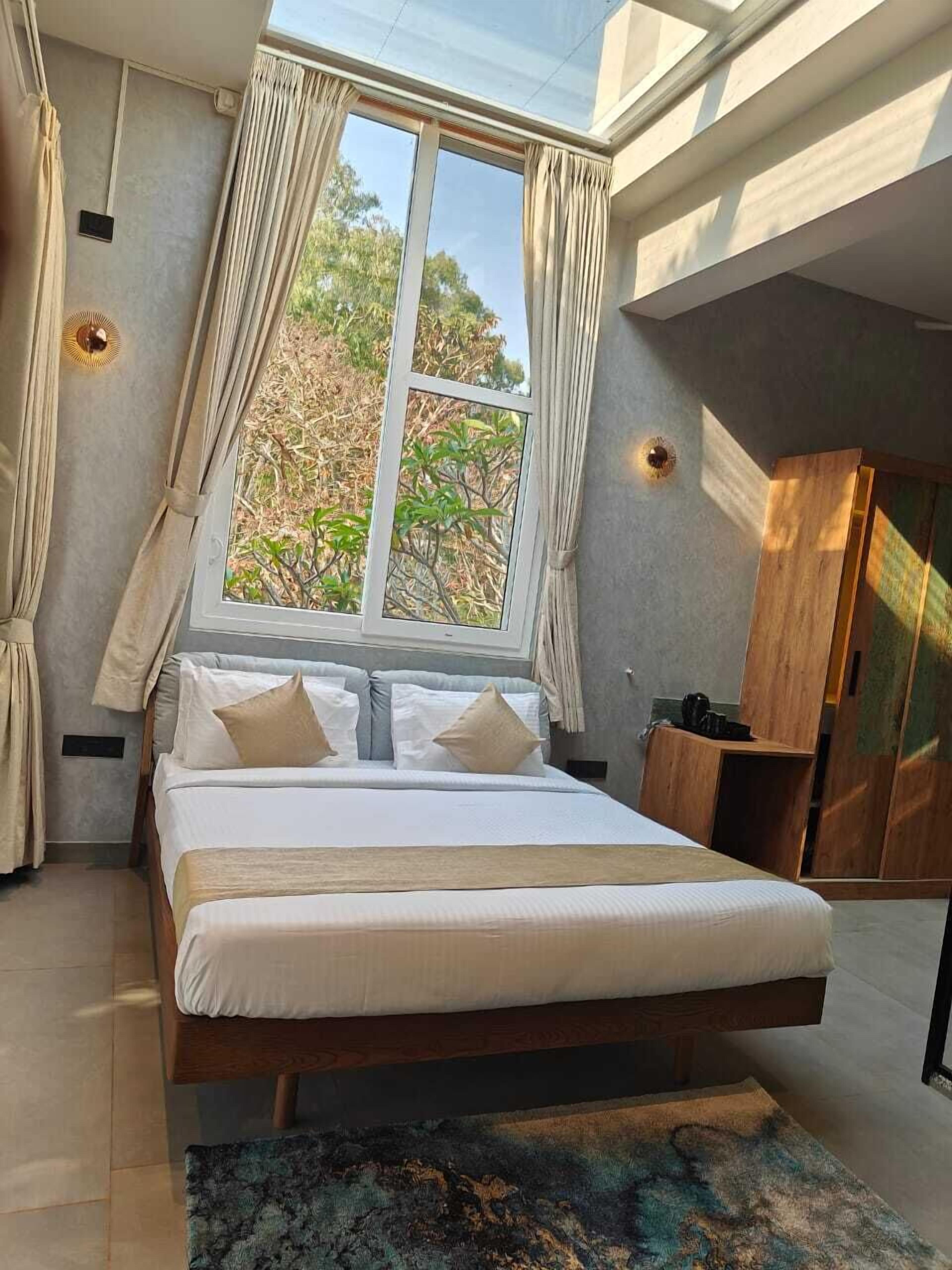 A bedroom with a large bed, a skylight, curtains, and a view of trees outside.