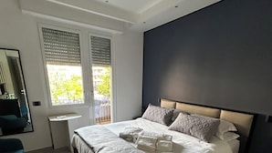 Un dormitorio moderno con una cama grande, una mesita de noche, una silla y una ventana con persianas.