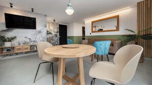 Un salon moderne avec une table ronde en bois, deux chaises, un canapé et un téléviseur fixé au mur.