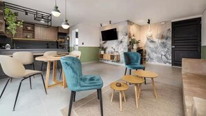 Un salon moderne avec un coin cuisine, comprenant un ensemble de salle à manger, des canapés et un téléviseur fixé au mur.