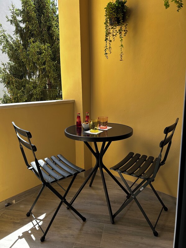 A small outdoor dining area with two chairs and a table, a hanging plant, and a bottle of Coca-Cola.
