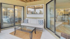 Una habitación soleada con un sofá blanco, una mesa de centro de vidrio y vistas a una casa a través de un ventanal.