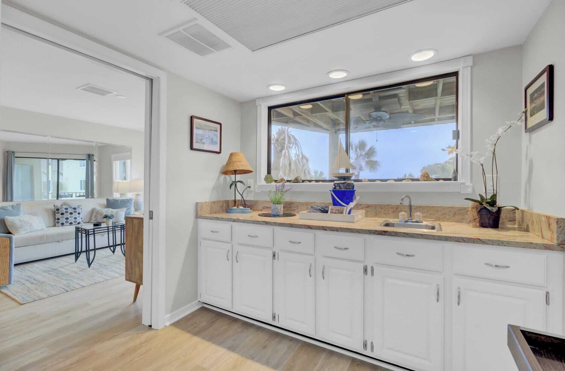 A modern kitchen with white cabinets, a large window with a view, and a dining area with a sofa and table.