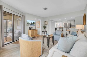 A modern living room with a sofa, a wicker chair, a coffee table, and a television mounted on the wall.