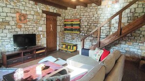 A cozy living room with a stone wall, wooden beams, a television, a sofa, and a staircase. - Το Erymanthos country home είναι μια πέτρινη μεζονέτα για στιγμές χαλάρωσης (Skepasto)