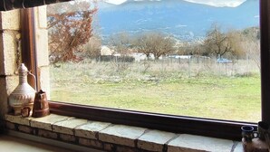 A window with a view of a grassy field, trees, and mountains in the distance. - Το Erymanthos country home είναι μια πέτρινη μεζονέτα για στιγμές χαλάρωσης (Skepasto)