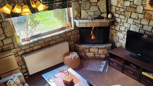 A cozy living room with a stone fireplace, a sofa, a coffee table, and a TV. - Το Erymanthos country home είναι μια πέτρινη μεζονέτα για στιγμές χαλάρωσης (Skepasto)
