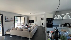 Ein modernes Wohnzimmer mit einer Couch, einem Esstisch und einer Küchenzeile mit Geräten.