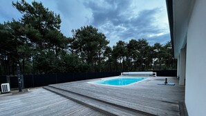 Eine Holzterrasse mit Schwimmbecken, umgeben von Bäumen und einem Zaun.