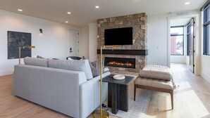 A modern living room with a stone fireplace, a grey sofa, a small table, and a cushioned bench.