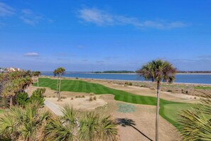 A golf course with a water body in the background, surrounded by palm trees and a clear sky. - 202 F Port O Call by Avantstay Amazing Oceanfront Views! (Isle of Palms)