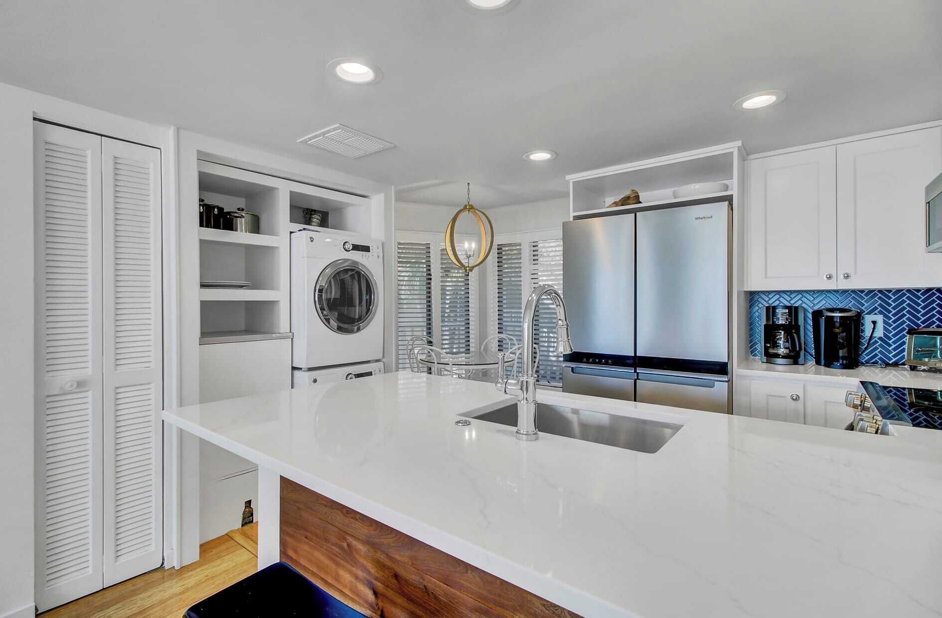 A modern kitchen with a central island, built-in appliances, and a blue patterned backsplash.