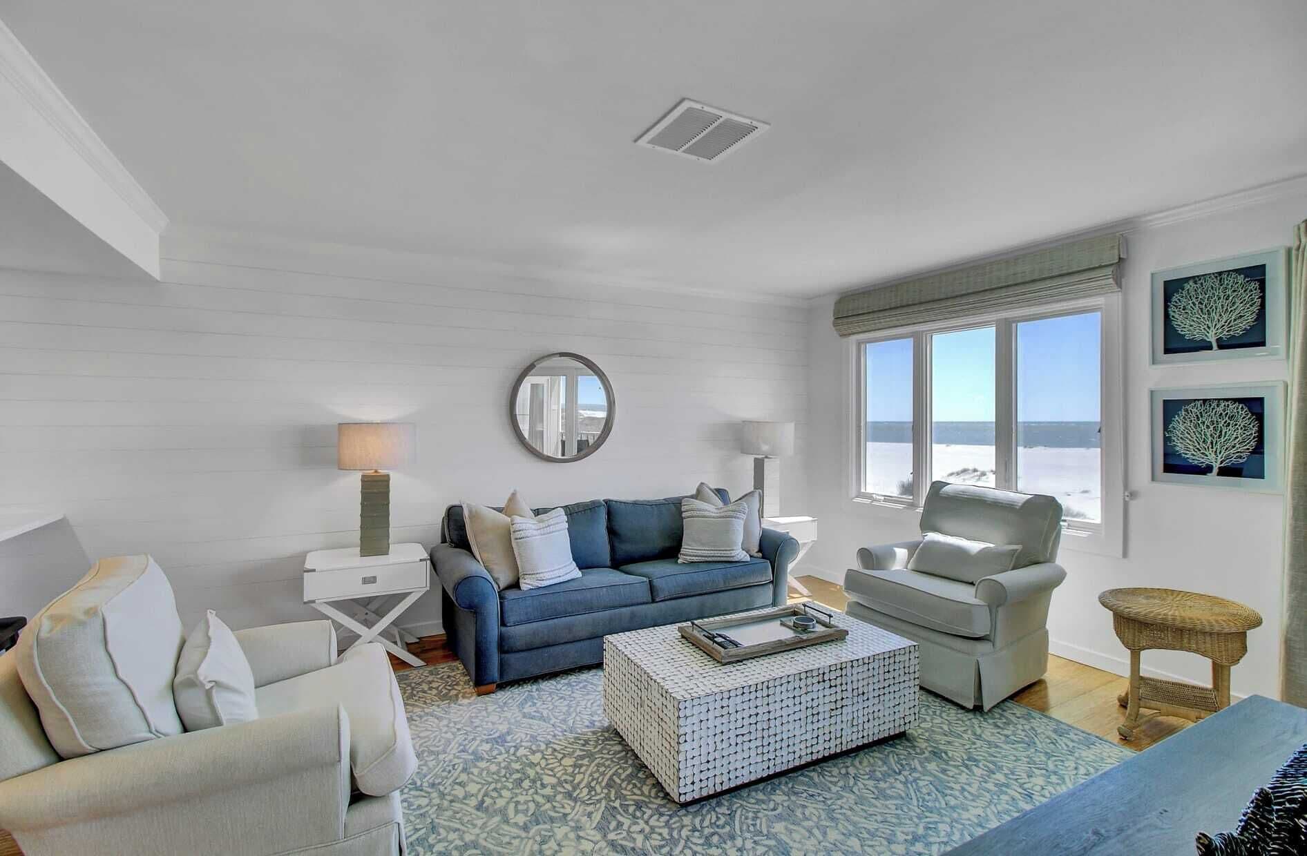 A living room with a blue sofa, a white armchair, a coffee table, and a view of the sea through large windows.