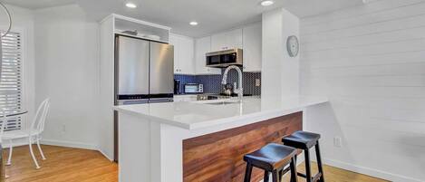 A modern kitchen with a white island, stainless steel appliances, and a wooden accent wall.