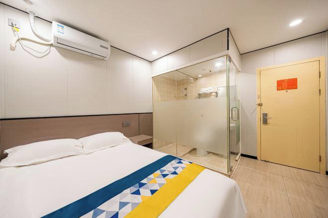 A hotel room with a bed, a glass shower enclosure, an air conditioning unit, and a door with a sign.
