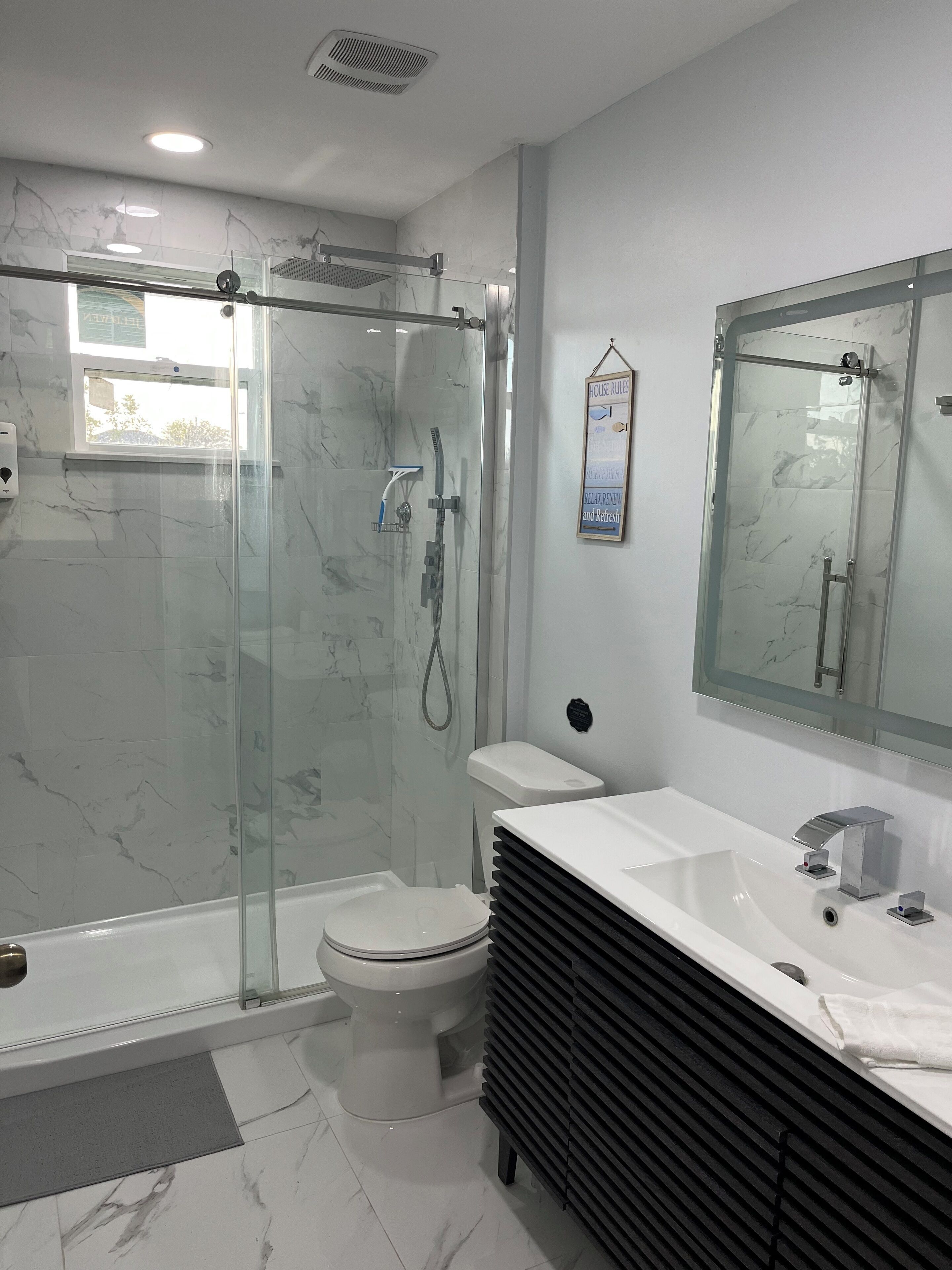 Ein modernes Badezimmer mit einer Glaskabine zur Dusche, einer weißen Toilette und einem Waschtisch mit großem Spiegel.