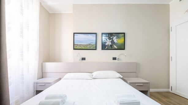 Ein modernes Hotelzimmer mit einem großen Bett, zwei Nachttischen, einer Kopfteil mit integriertem Fernseher und zwei gerahmten Bildern an der Wand.