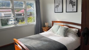 A bedroom with a bed, a nightstand, a lamp, a window with curtains, and two framed pictures on the wall.
