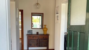 A hallway with wooden flooring, a green door, a mirror, a cabinet, and a rug.