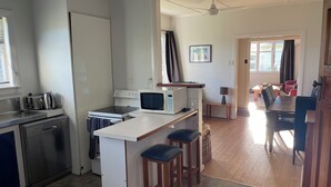 A compact kitchen with a microwave, toaster, and dishwasher. There is a small bar stool area and a dining table with chairs.