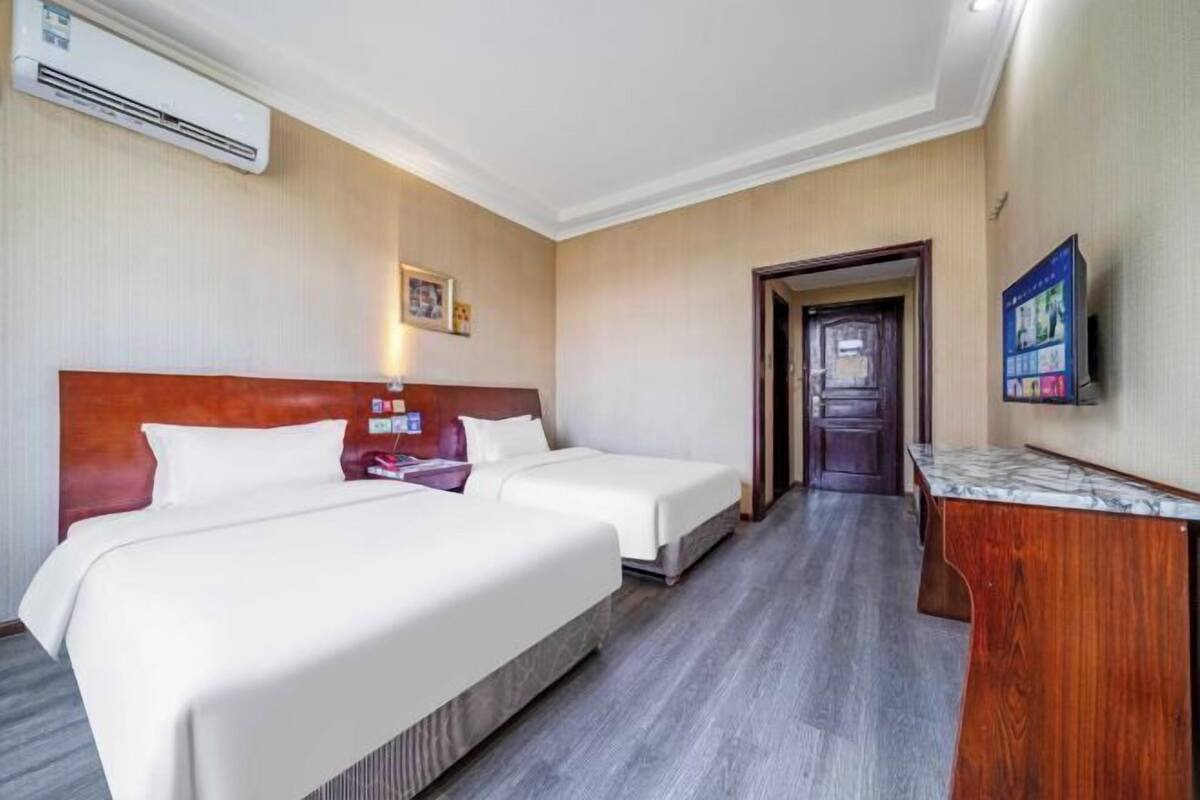 A hotel room with two beds, a wooden headboard, a desk, and a TV on the wall.