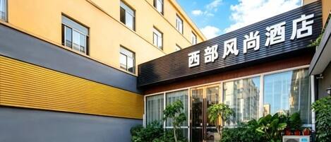 A hotel entrance with a modern facade, large windows, and a red carpet leading to the door.