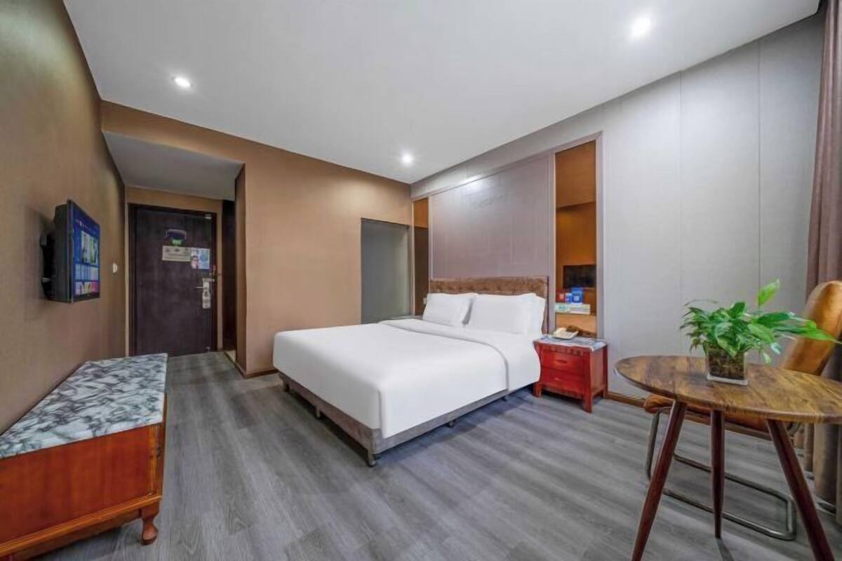 A hotel room with a bed, bedside table, chair, and a small table with a plant.