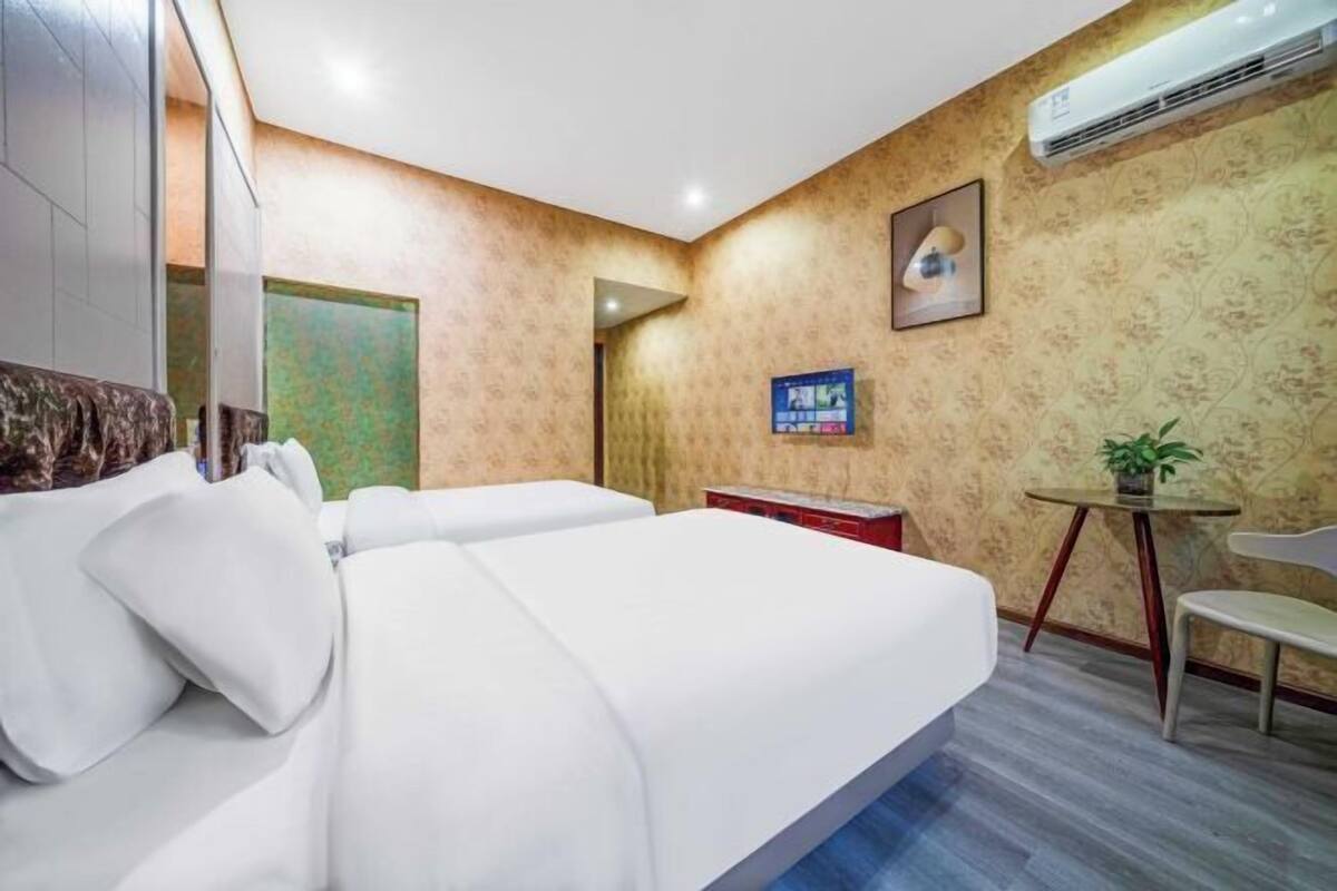 A hotel room with two beds, a small table, a chair, an air conditioner, and a framed picture on the wall.