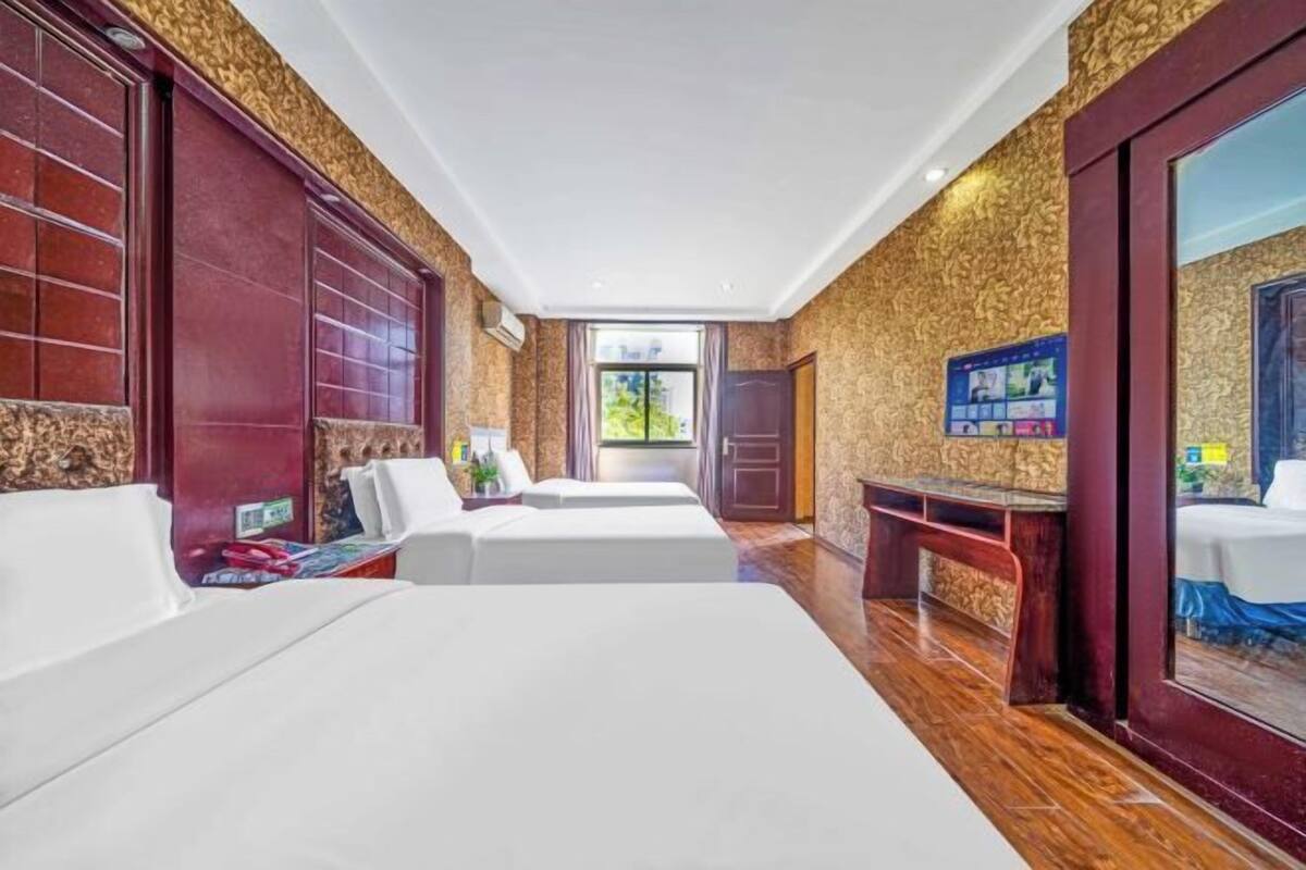 A hotel room with two beds, a wooden bench, a small table, and a large mirror.