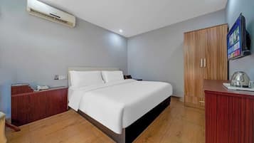 A bedroom with a bed, wooden wardrobe, a desk, and an air conditioning unit.