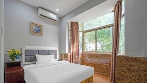 A hotel room with a bed, an air conditioner, a nightstand, a window with curtains, and a view of greenery outside. - Taizhou Western Style Hotel (Taizhou)