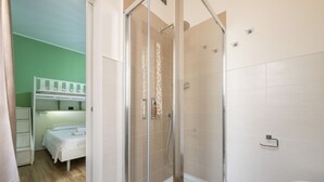 Une chambre avec un lit superposé, une douche fermée par des parois de verre et des toilettes blanches.
