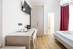 A modern hotel room with a bed, a desk with a chair, a television mounted on the wall, and a wardrobe. - Estay Piazza Repubblica - Suite Mirto (Cagliari)
