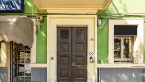 A building with a green facade, a double wooden door, and a window with a view of trees.