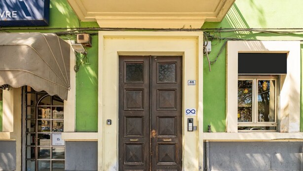 Ein Gebäude mit grüner Fassade, einer zweiflügeligen Holztür und einem Fenster mit Blick auf Bäume.