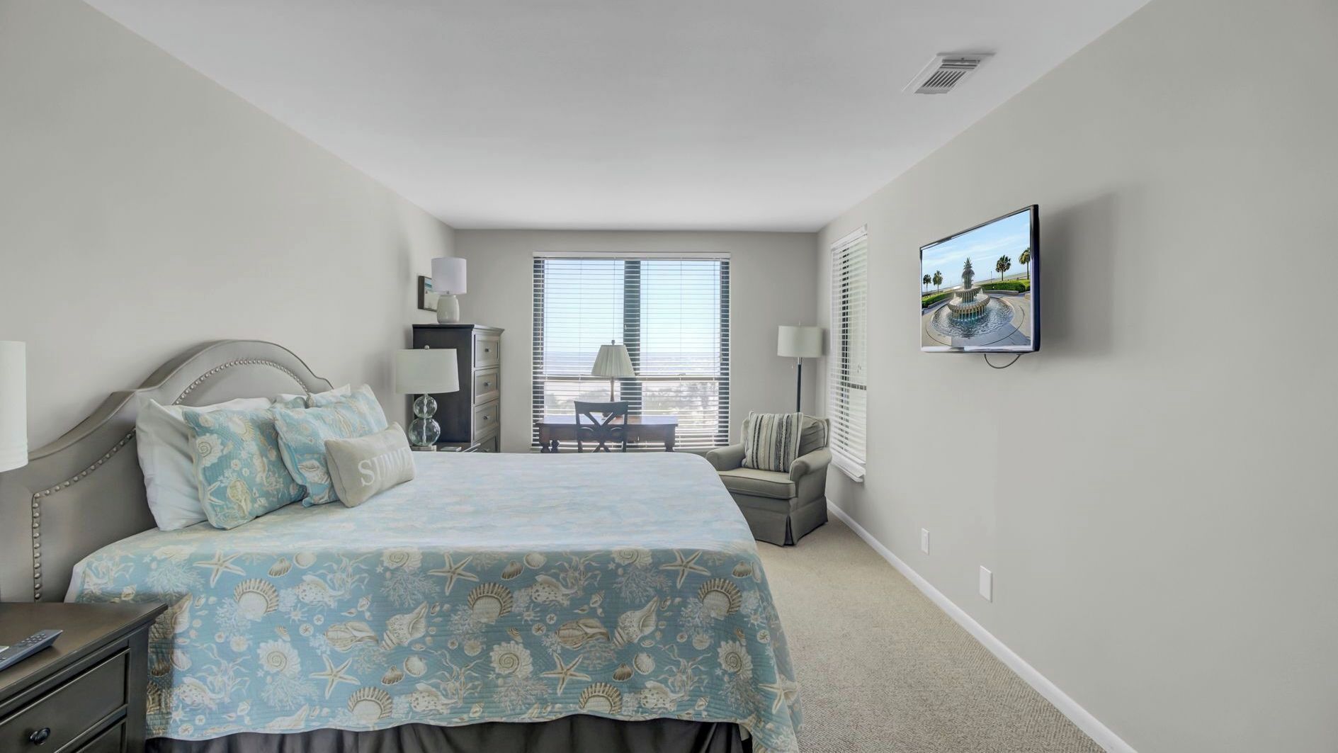 A bedroom with a bed, bedside tables, a TV, a window with blinds, and a view of the outdoors.