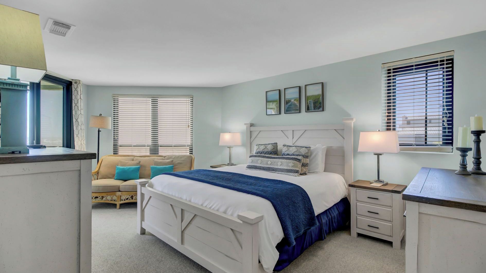 A bedroom with a bed, bedside tables, a nightstand, a sofa, and a window with blinds.
