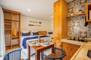 Habitación de hotel pequeña con cama, una mesa de comedor junto a sillas, kitchenette y un armario de madera.