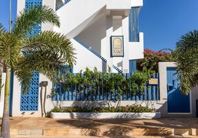 Um edifício branco com detalhes em azul e uma placa com a inscrição "Vila Maria".