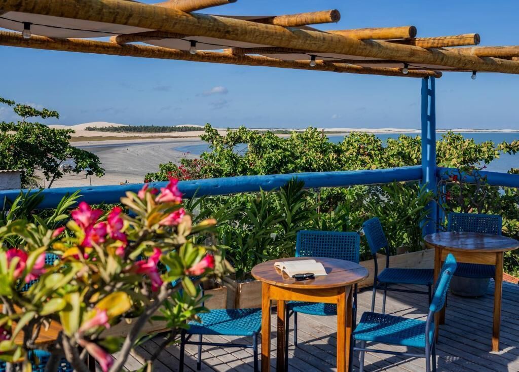 Ein Außenbereich mit Blick auf den Strand, ausgestattet mit Holztischen und -stühlen, einer Pergola und üppigem Grün.